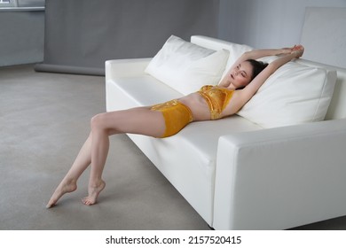 Slender Beautiful Brunette Girl In Yellow Velvet Lingerie Resting On A White Sofa.