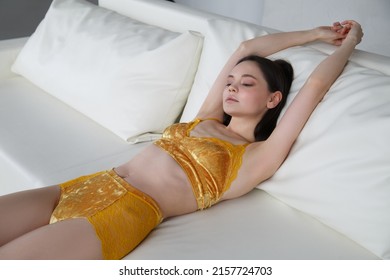 Slender Beautiful Brunette Girl In Yellow Velvet Lingerie Resting On A White Sofa.