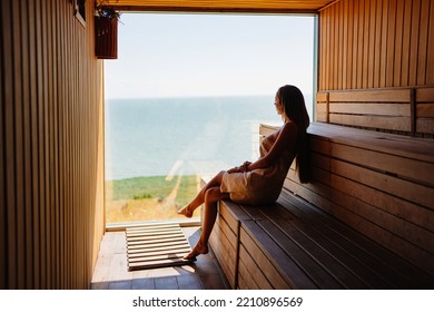 a slender and beautiful young woman in a towel sits on a bench in the sauna with the panoramic window. relax in the spa center. tourism and travel. - Powered by Shutterstock