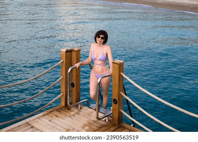 A slender brunette woman rises from sea along the stairs pier.