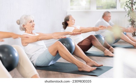 Slender elderly woman practicing pilates with soft ball in training area during pilates classes - Powered by Shutterstock