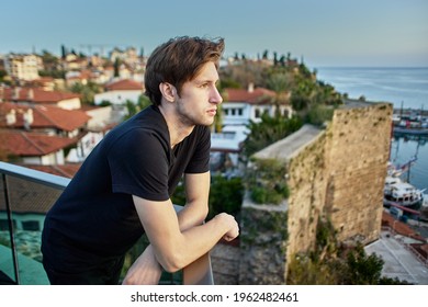 Slender European man, about 20 years old, sadly looks at old city in Antalya from observation point.