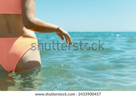 A slender girl, facing away from the camera, stands in the azure sea wearing a swimsuit, epitomizing serene beachside beauty. Stock photo © 