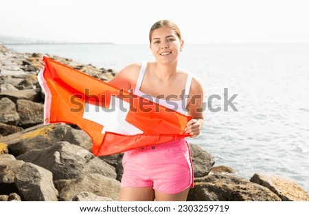 Slender girl with the flag of Switzerland on the lakeshore on a sunny summer day