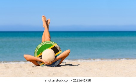 A slender girl on the beach in a straw hat in the colors of the Tanzania flag. The concept of a perfect vacation in a resort in the Tanzania and Zanzibar. Focus on the hat.