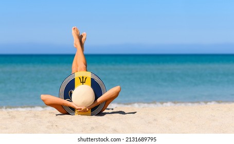 A Slender Girl On The Beach In A Straw Hat In The Colors Of The Barbados Flag. The Concept Of A Perfect Vacation In A Resort In The Barbados. Focus On The Hat.