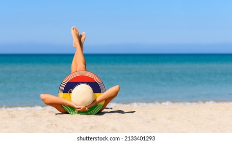 A slender girl on the beach in a straw hat in the colors of the Mauritius flag. The concept of a perfect vacation in a resort in the Mauritius. Focus on the hat. - Shutterstock ID 2133401293