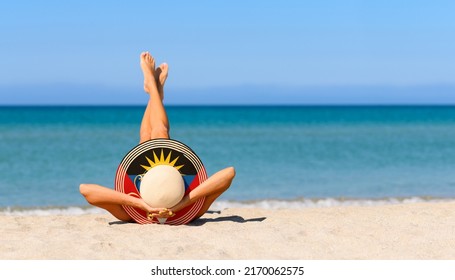 A Slender Girl On The Beach In A Straw Hat In The Colors Of The Antigua And Barbuda Flag. The Concept Of A Perfect Vacation In A Resort In The Antigua And Barbuda. Focus On The Hat.