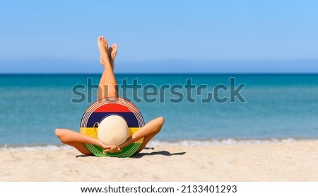 A slender girl on the beach in a straw hat in the colors of the Mauritius flag. The concept of a perfect vacation in a resort in the Mauritius. Focus on the hat.