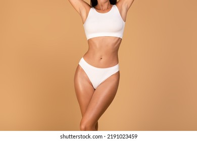 Slender lady with hands up posing in white underwear over beige studio background, showing her beautiful curves, copy space. Diet, athletic body concept