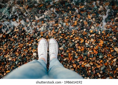 slender legs in blue jeans and white stylish sneakers on rocky beach and wave rolls over your feet. - Powered by Shutterstock