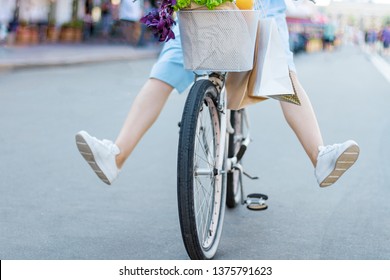 Slender Legs Of Young Woman, In Blue Dress On Female Bicycle. Girl Is Ridding Around City On White Bike. Vintage Retro  Bicycle With Basket Of Groceries And Shopping Bags On Handlebars. 