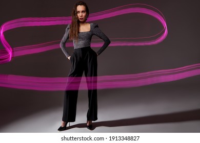 slender model against the backdrop of purple freezelight lines, attractive lady in dress posing isolated over dar studio background