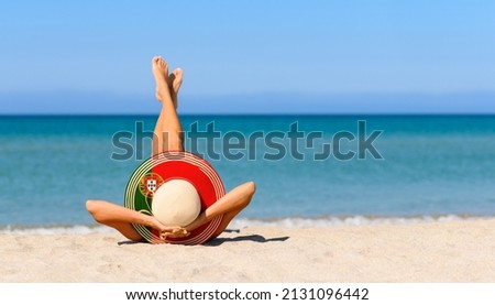 A slender tanned girl on the beach in a straw hat in the colors of the flag of Portugal. The concept of a perfect vacation in a resort in the Portugal. Focus on the hat.