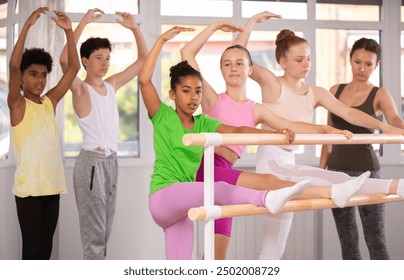 Slender teenage girls doing leg stretching exercise holding by ballet barre during workout session in group - Powered by Shutterstock