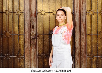 Slender Teenager Girl With Short Shaved Hair, In Casual Summer Clothes, Posing Near Ancient Gate. Slender Model With Trendy Hairstyle Of Teenage Generation Z Posing Near Vintage Door