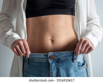 A Slender Woman With A Bare Stomach Shows How She Lost Weight. Jeans Have Become Too Big. The Concept Of Diet And Healthy Eating