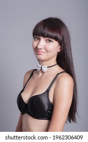A slender woman dressed in black bra and bow tie only on gray background