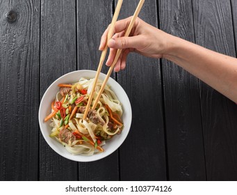 Slender Woman Hand With Chop Sticks In Bowl Of Traditional Asian Udon Noodles On Black Background Minimalist Style Top View