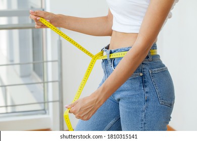 Slender woman in jeans and a white T-shirt measures her waist - Powered by Shutterstock