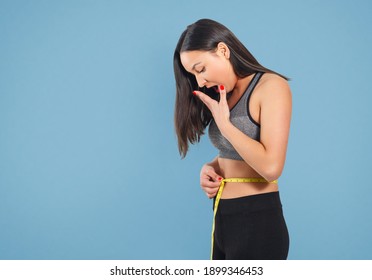 A slender woman measures her waist with a measuring tape. Against a blue background.