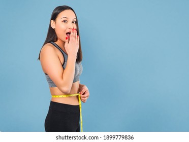 A slender woman measures her waist with a measuring tape. Against a blue background.
