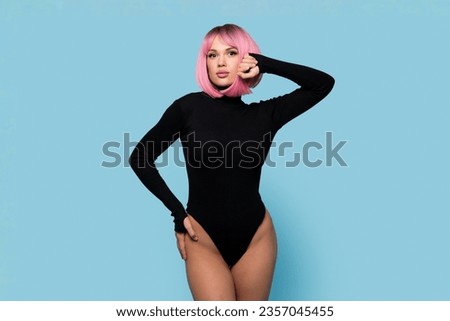Slender woman posing in pink wig and black bodysuit on blue background. Portrait of gorgeous trendy girl. Healthy, smooth and tanned skin. Perfect female body