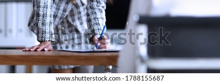 Slender woman stands in office and signs document. Employee training, continuing education. Professional career, growth and promotion. Convey to others your words and emotions. Work subordinates Foto stock © 