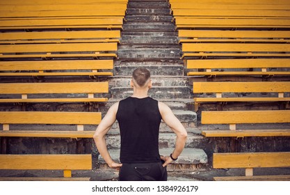 A slender young man in black sportswear stands in front of the stairs stadium stands. ready for action, step to victory, challenge. - Shutterstock ID 1384926179