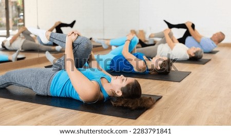 Slender young woman practicing pilates on gray mat in exercise room during pilates classes. Persons doing pilates in fitness hall