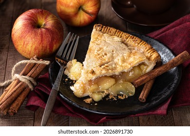 Slice Of Apple Pie On A Plate With Apples And Cinnamon Sticks In Background