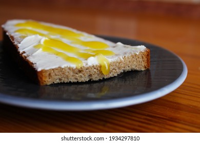 A Slice Of Bread, Spread With Cheese And Butter, Sprinkled With Yellow Syrup With Honey On A Plate. Well-fed Breakfast. Selective Focus And Blurred Background.