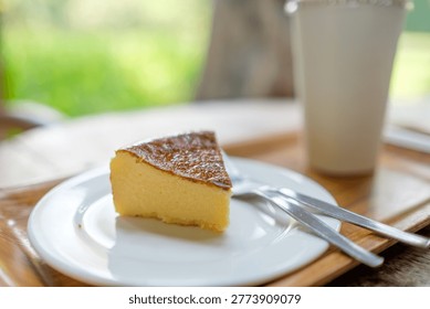 Slice of burnt basque cheesecake served on a wooden tray with a refreshing drink and a vintage style camera in a blurred cafe garden setting.