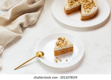 Slice of carrot cake with coconut cream and walnuts on a white plate. Raw cake, no baked goods. Sugar, gluten and lactose free.
