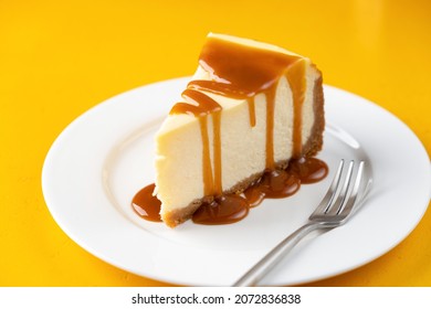 Slice Of Cheesecake With Salted Caramel Sauce On Plate, Isolated On Yellow Background