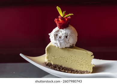 Slice of cheesecake topped with a scoop of ice cream and carved strawberry garnish on a moody glass table with soft bokeh and romantic lighting