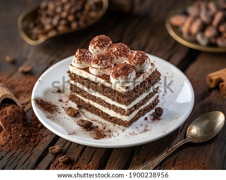 Slice of chocolate cake with tiramisu cream and cocoa powder on wooden table.