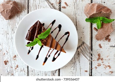 Slice of chocolate cheesecake on plate, above view over a rustic white wood background