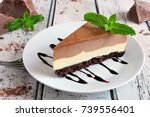 Slice of chocolate vanilla cheesecake on plate against a rustic white wood table
