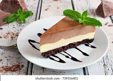 Slice of chocolate vanilla cheesecake on plate against a rustic white wood table - Powered by Shutterstock