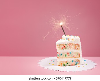 Slice of Colorful Birthday Confetti Cake with a lit sparkler over a pink background.