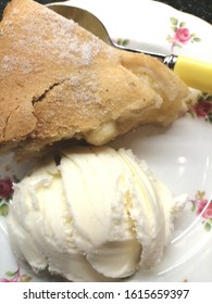 Slice Of Delicious Hot Apple Pie With A Dollop Of Ice Cream On A Pretty Floral China Plate With A Yellow Handled Spoon On A Dark Background. 