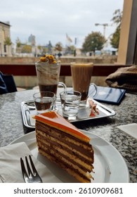 Slice of Dobos layered cake served with lattes and whipped cream coffee in a cozy Budapest café. Perfect for dessert and coffee lovers.