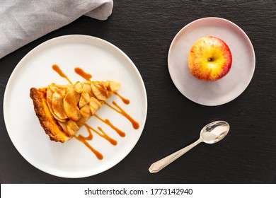 Slice Of French Apple Tart, An Open Faced Apple Pie, Aside A Gala Apple In A Small Grey Plate, A Vintage Retro Silver Spoon And A Grey Linen Napkin On A Grey Slate Background. Flat Lay, Top View.