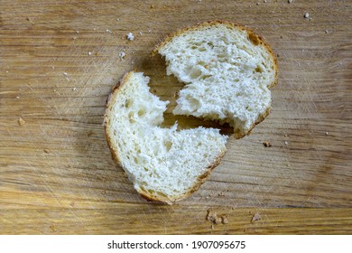Slice of fresh bread loaf on cutting board. Piece of bread is broken into two pieces.  Symbolizes discord, rift, split, break. Top view. Close-up. Selective focus. Copy space. 