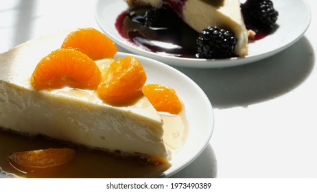 Slice Of Homemade Cheese Cake With An Almond Meal Crust Topped With Mandarin Oranges With An Orange Sauce Pour And A Blackberry Topped Piece 