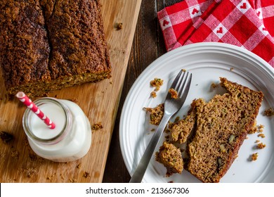 Slice of homemade zucchini bread sitting on white plate with fork and glass of milk with red heart straw and napkin