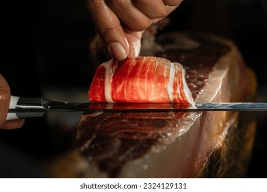 Slice of Iberian ham from Spain 100% acorn-fed, cut with a knife by a professional. Close up view of ham cutter typical of Spain gourmet product international sale