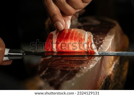 Slice of Iberian ham from Spain 100% acorn-fed, cut with a knife by a professional. Close up view of ham cutter typical of Spain gourmet product international sale