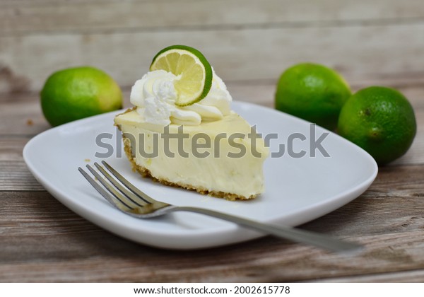 Slice of key lime pie\
on plate with limes